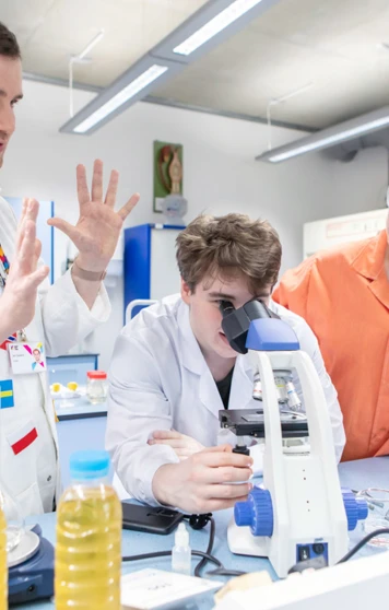 Science lecturer guiding a student on microscope use with classmates observing in the lab at Glasgow Kelvin College Science lecturer guiding a student on microscope use with classmates observing in the lab at Glasgow Kelvin College